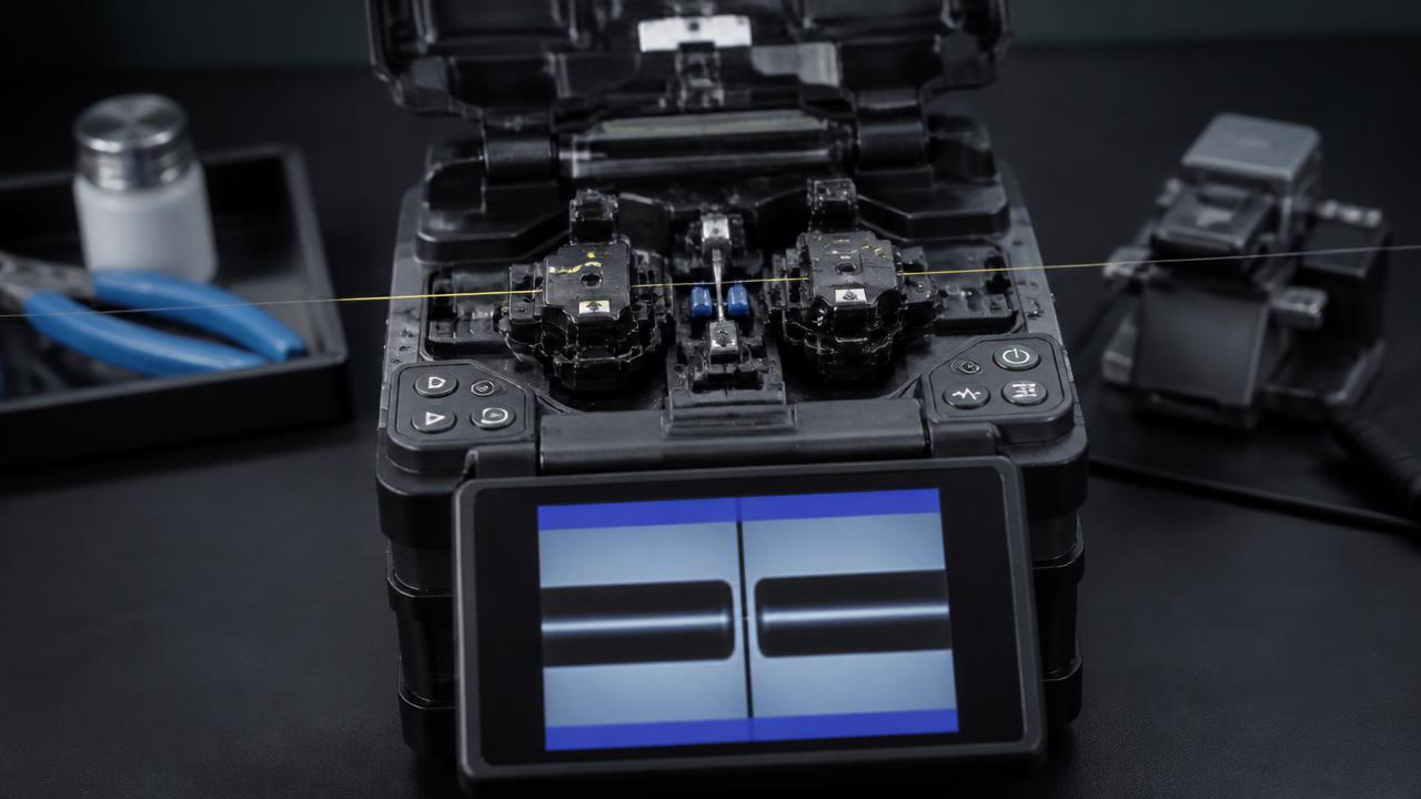 Open core-alignment fusion splicer with two bare optical fibers seated in the V-grooves and the alignment view shown on the splicer screen.